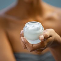 Closeup of african woman holding moisturizer cream jar. Detail of black hands holding face lotion. Woman showing white moisturiser for healthy skin.